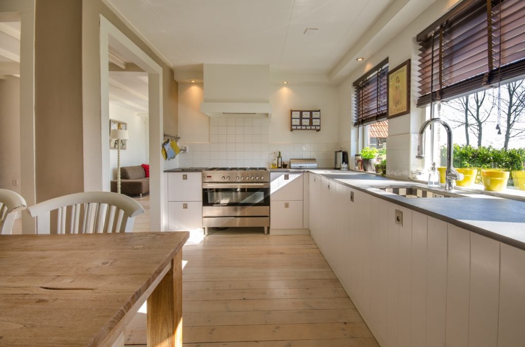 Kitchen with white cabinets, light wood flooring, accessible appliances and a wooden table